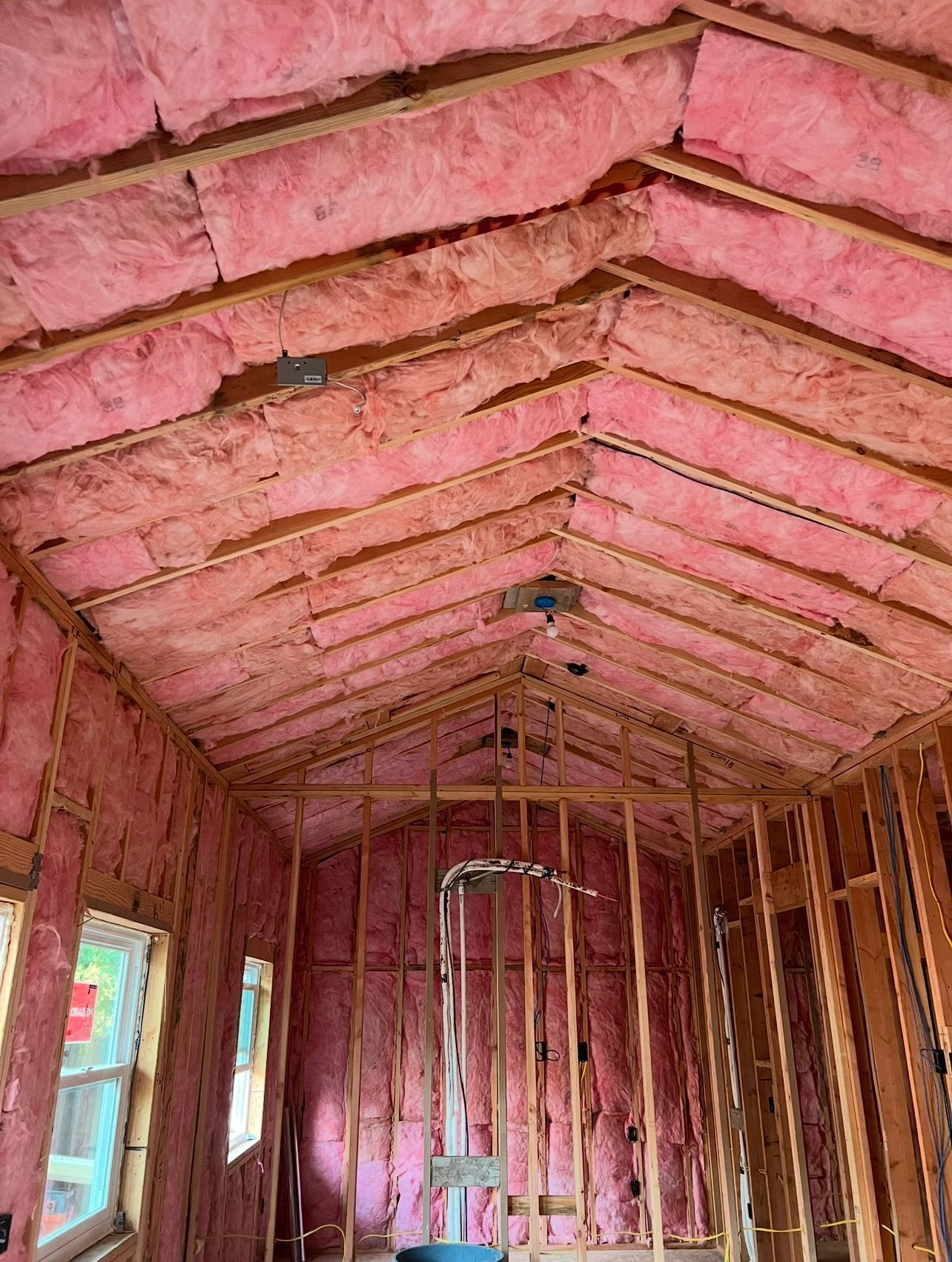 Interior of a building under construction, insulated with pink fiberglass. Wooden beams and frames are visible.