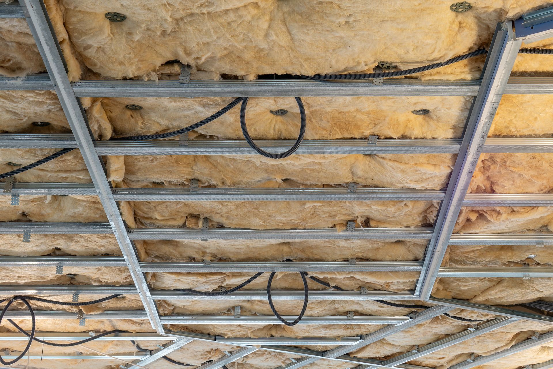 Metal grid ceiling framework with insulation and black electrical wiring.