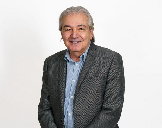 Smiling man in a gray blazer and blue shirt against a white background