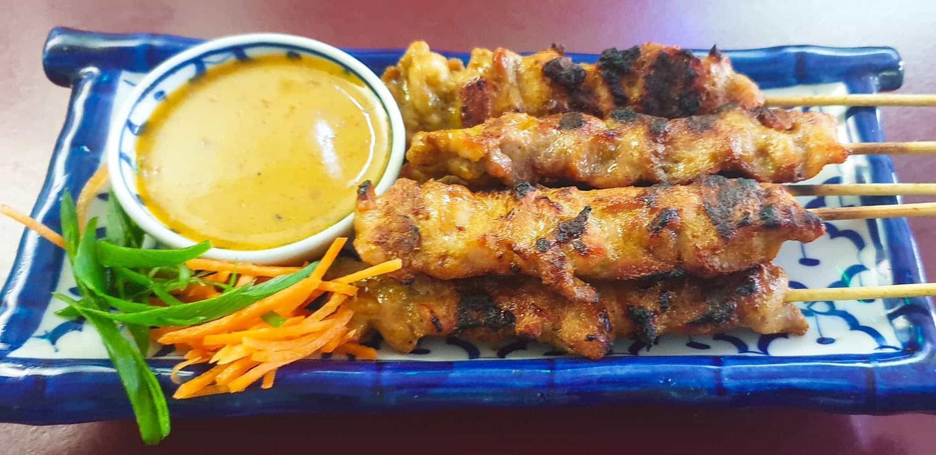 a Blue and White Plate Topped With Chicken Skewers and a Bowl of Dipping Sauce — Thai Satay Hut In Lismore, NSW