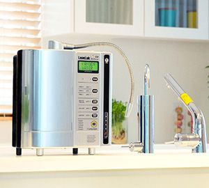 Water filtration system with four beige tanks, blue pipes, and a large blue water tank outdoors.