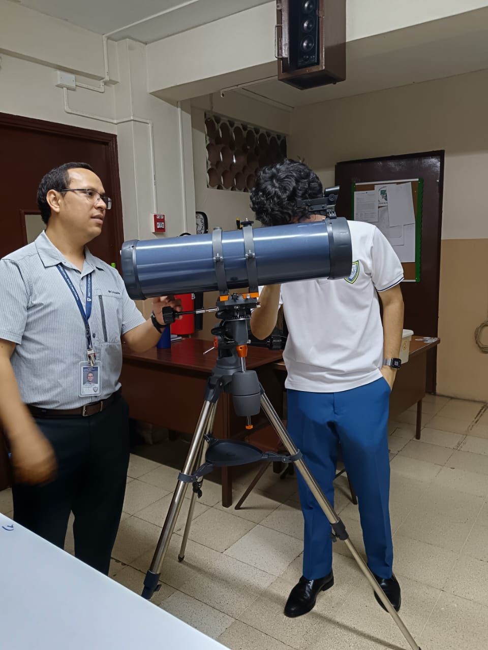 Dos hombres miran a través de un telescopio en una habitación.