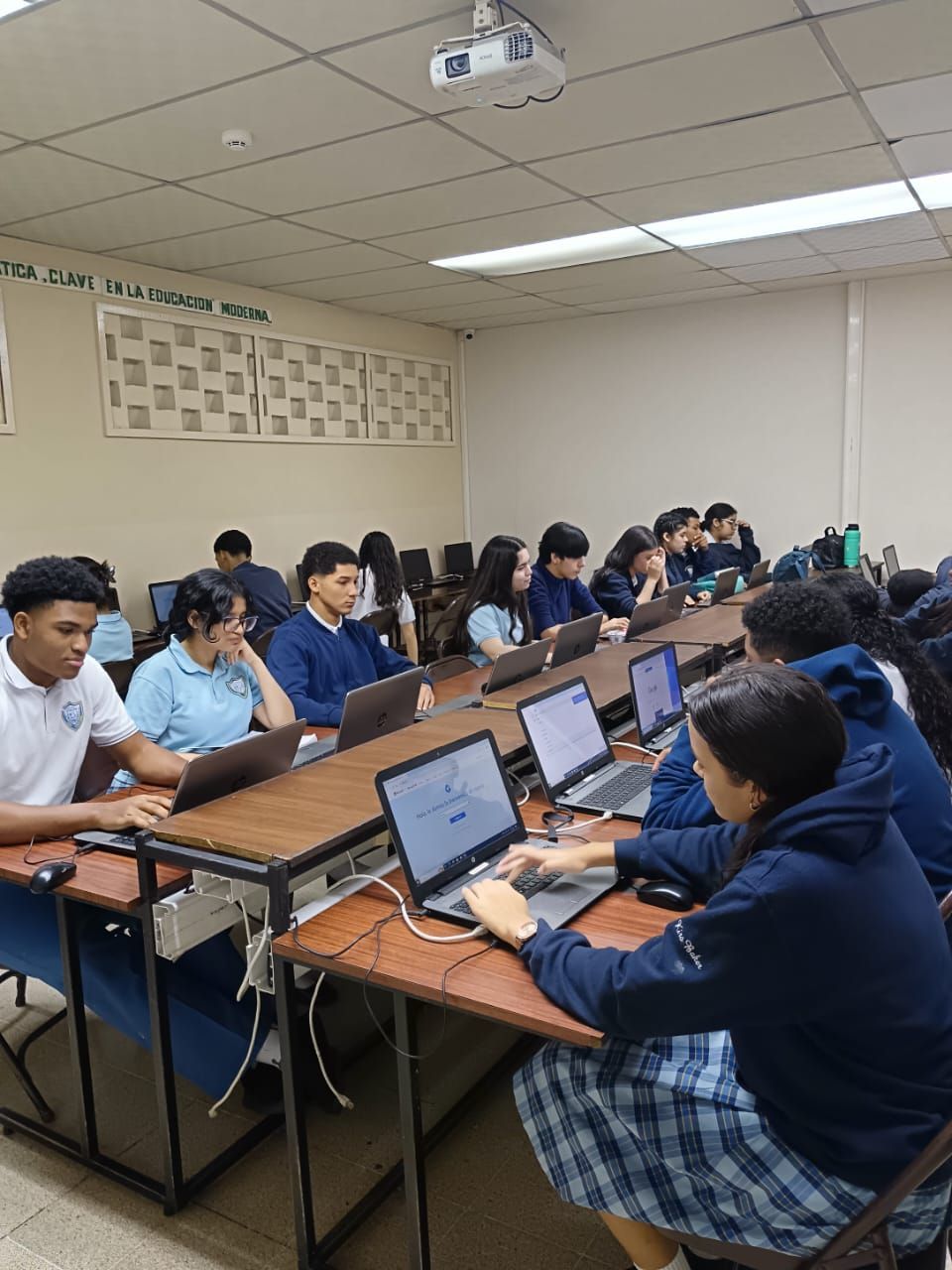 Un grupo de estudiantes está sentado en sus escritorios en un aula usando computadoras portátiles.