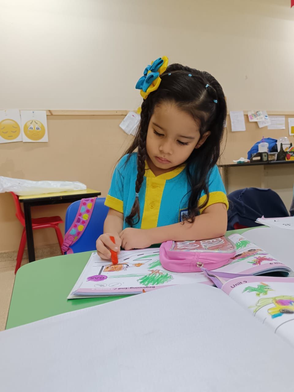 Una niña está sentada en una mesa en un aula con un estuche de lápices de color rosa.