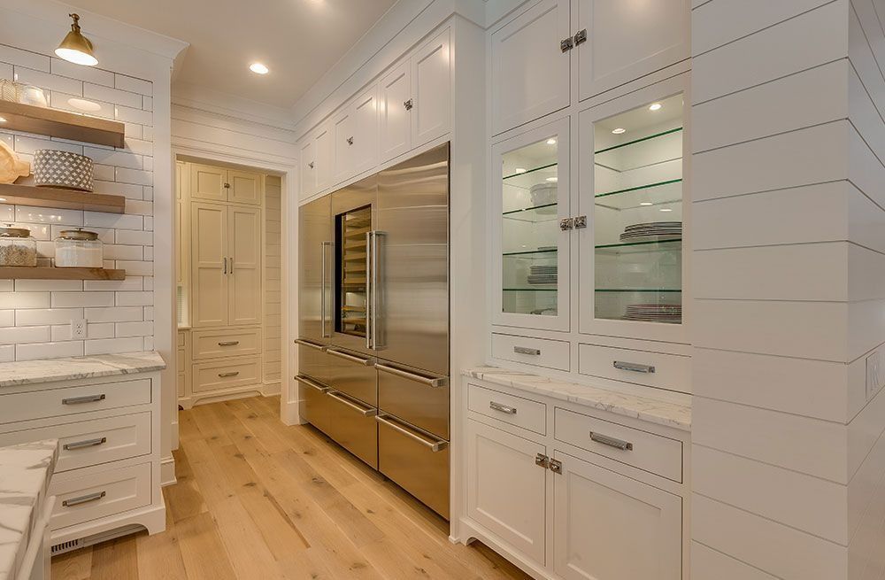 Bright white walk-in pantry with built-in cabinets, wood floors, and stainless steel appliances