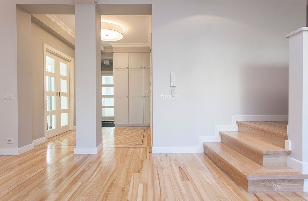 Bright empty hallway with wood floors, white walls, bathroom doorway, and carpeted stairs on the right
