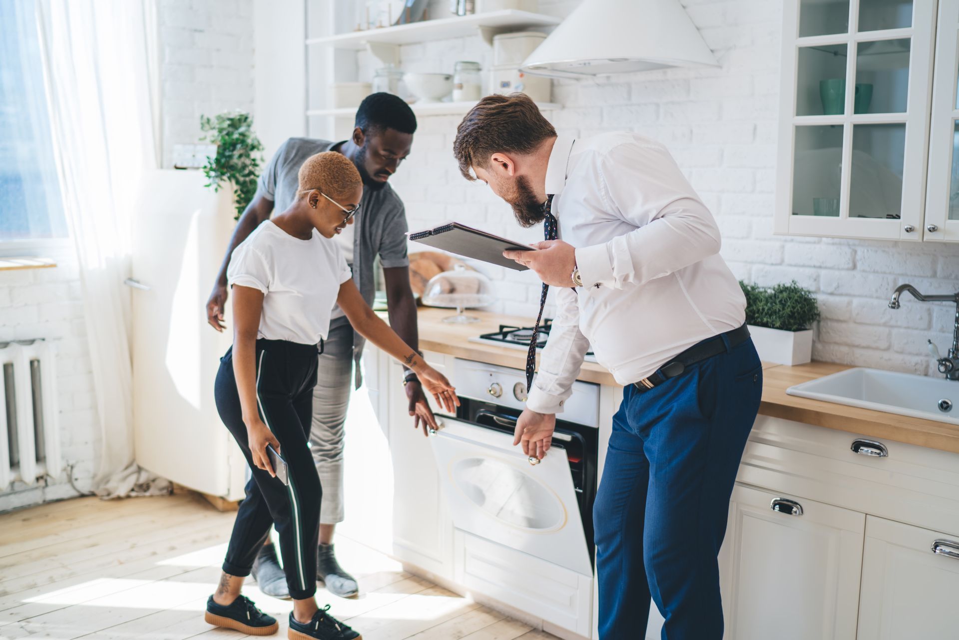 Three people in a bright kitchen looking at a tablet together