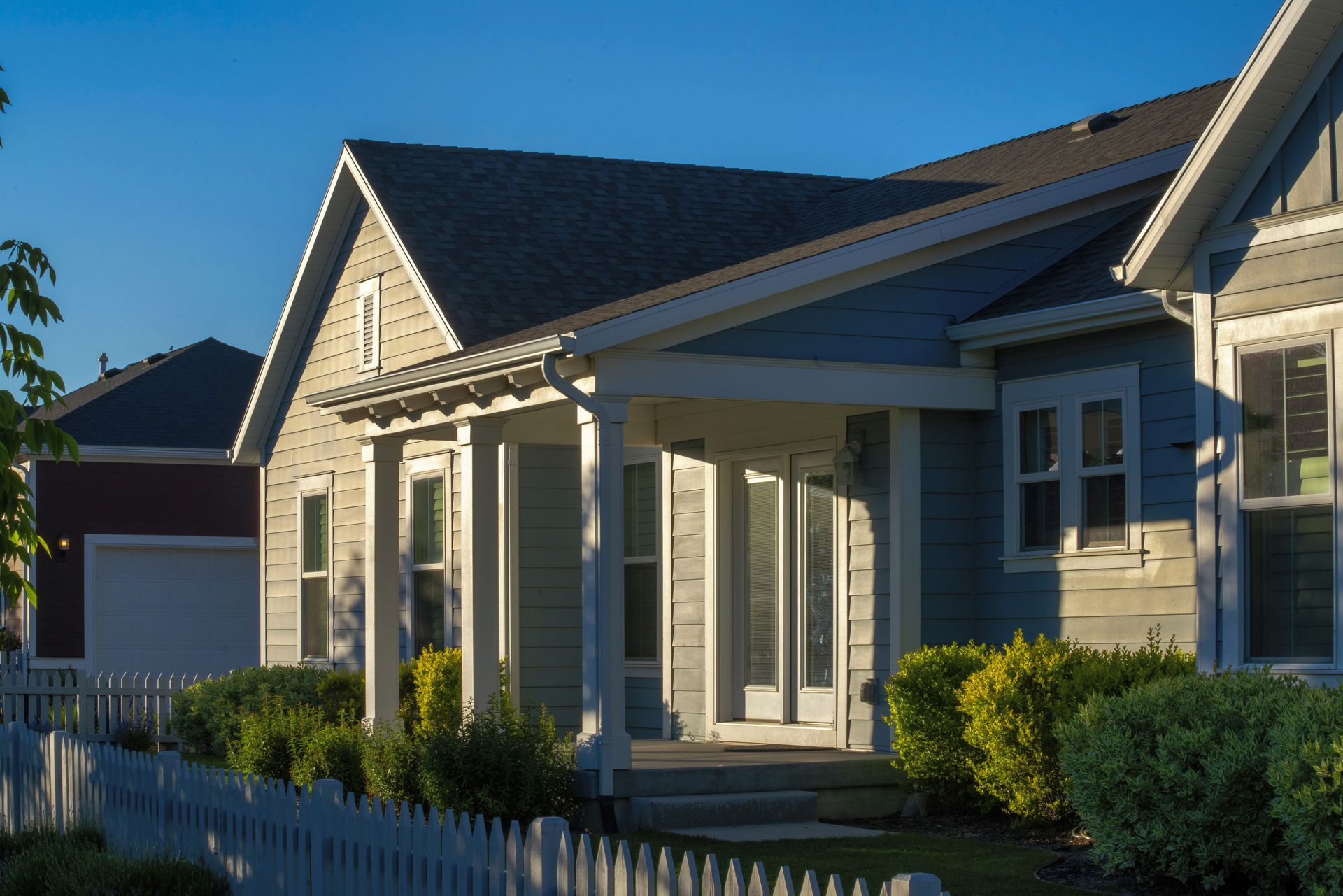 Suburban house with beige siding, white trim, front porch, and a garage in warm evening light