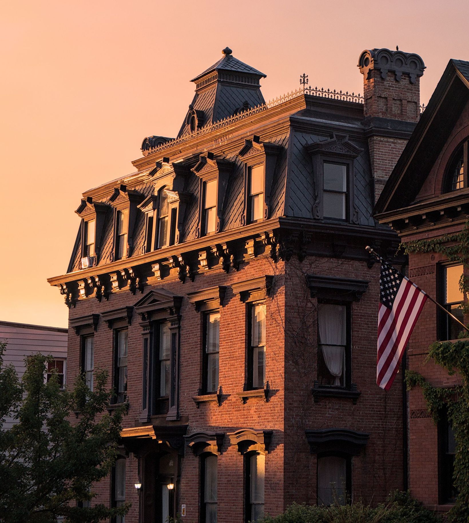 Historic brick building at sunset with ornate roof details and an American flag hanging outside