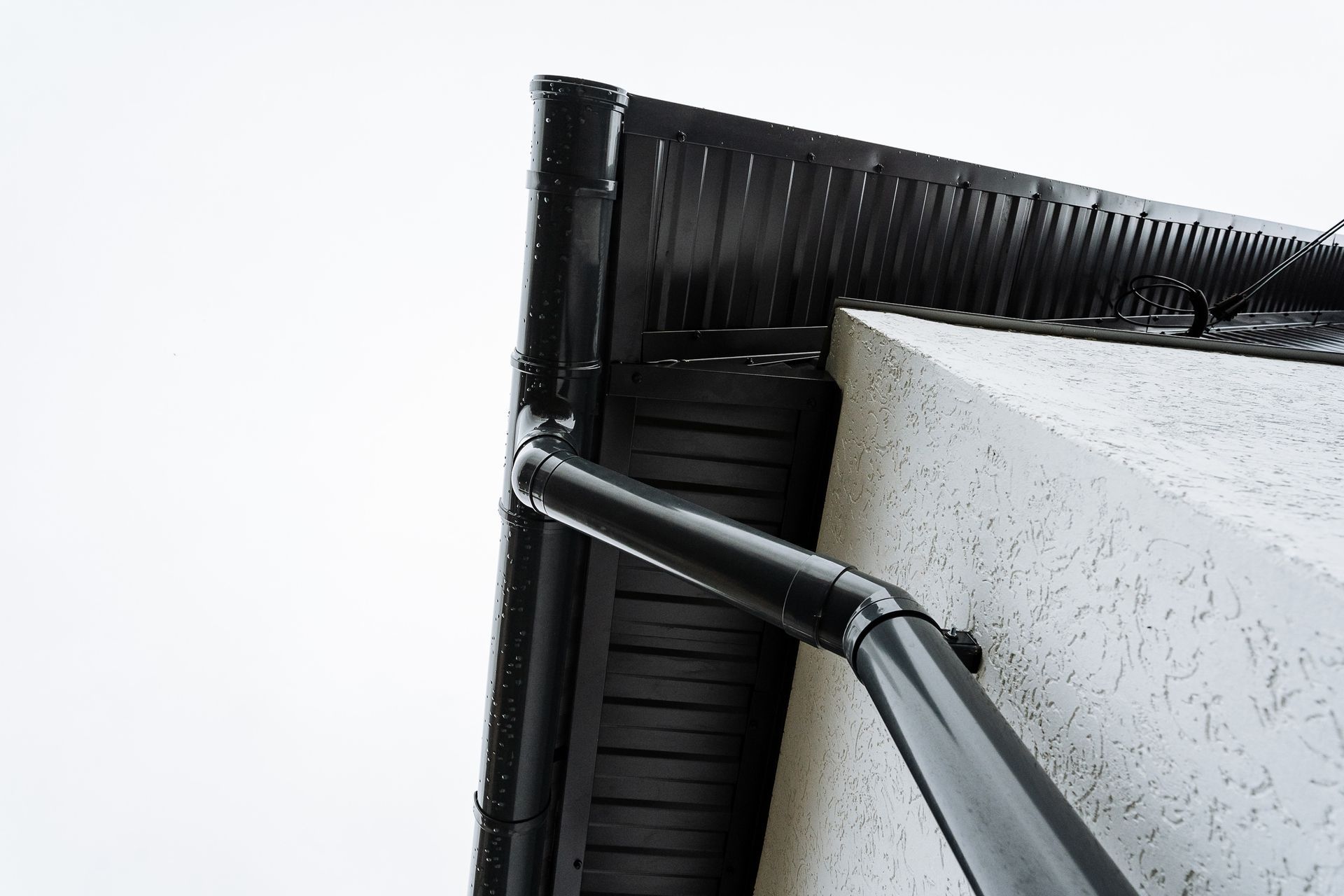 Black metal gutter and downspout on a white building corner