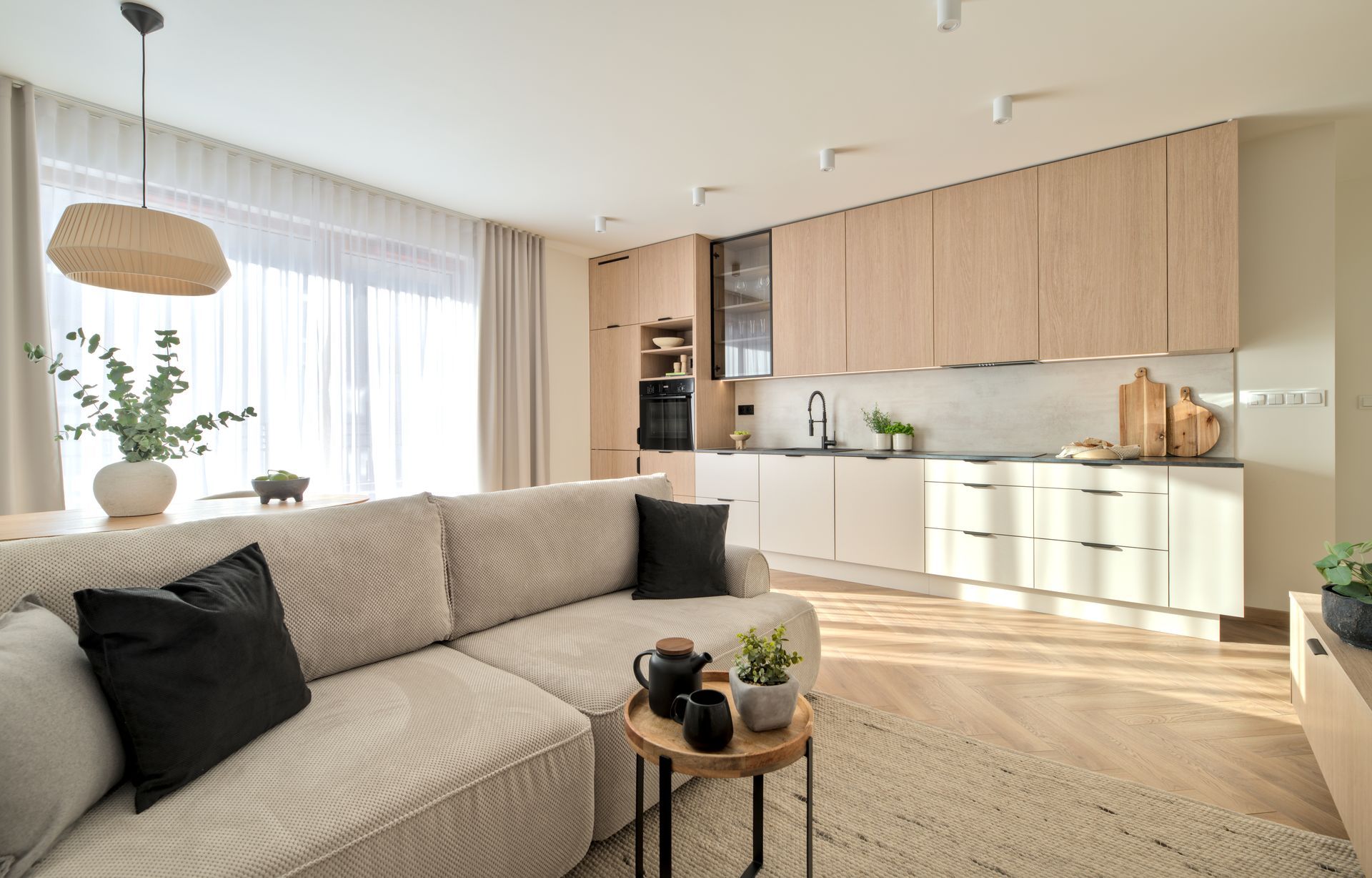 Bright modern living room with beige sofa, wood kitchen cabinets, and large windows