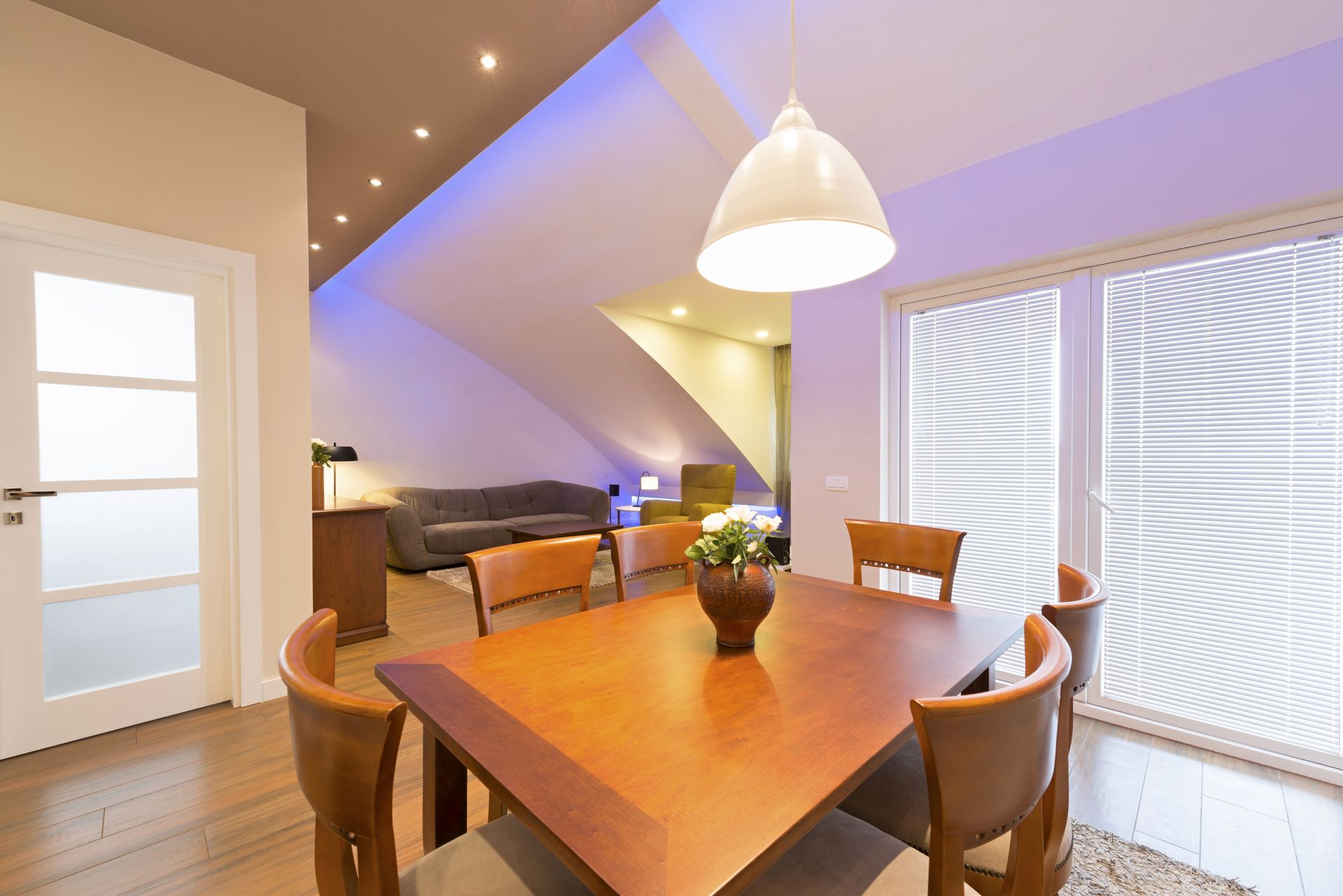 Cozy dining room with wooden table, pendant light, sofa, and large windows with blinds