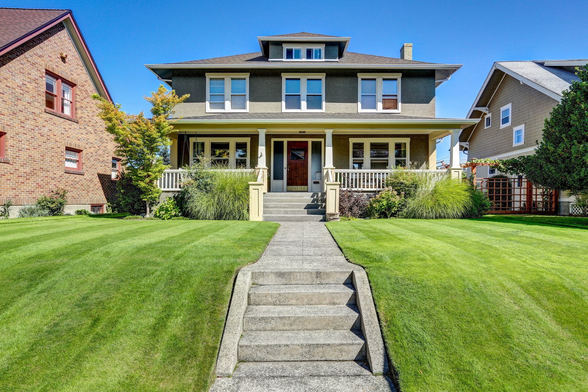 Two-story house with a front porch, stone steps, and a neatly mowed lawn under a clear blue sky