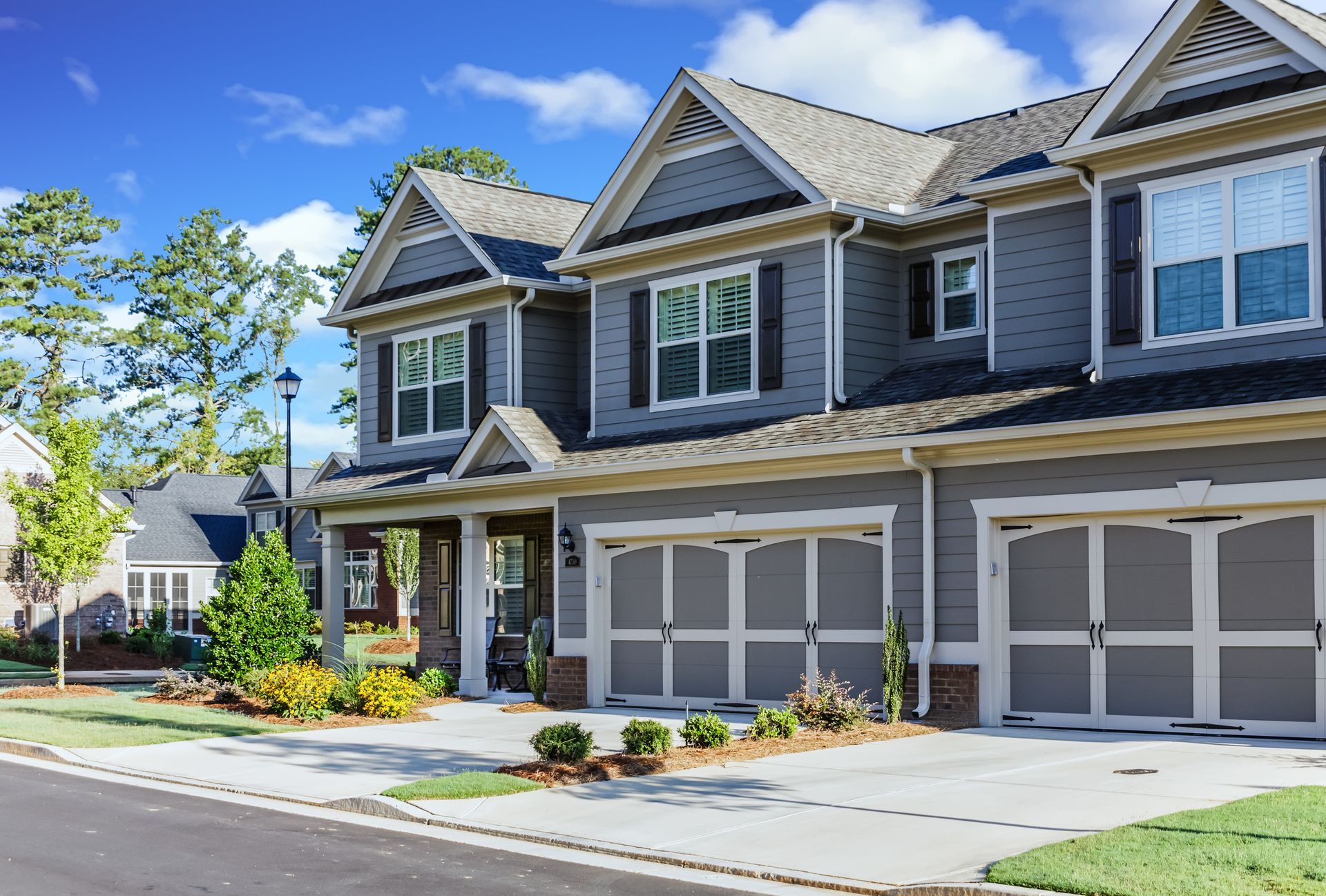 Row of gray suburban townhouses with garages and a landscaped front walkway on a sunny day