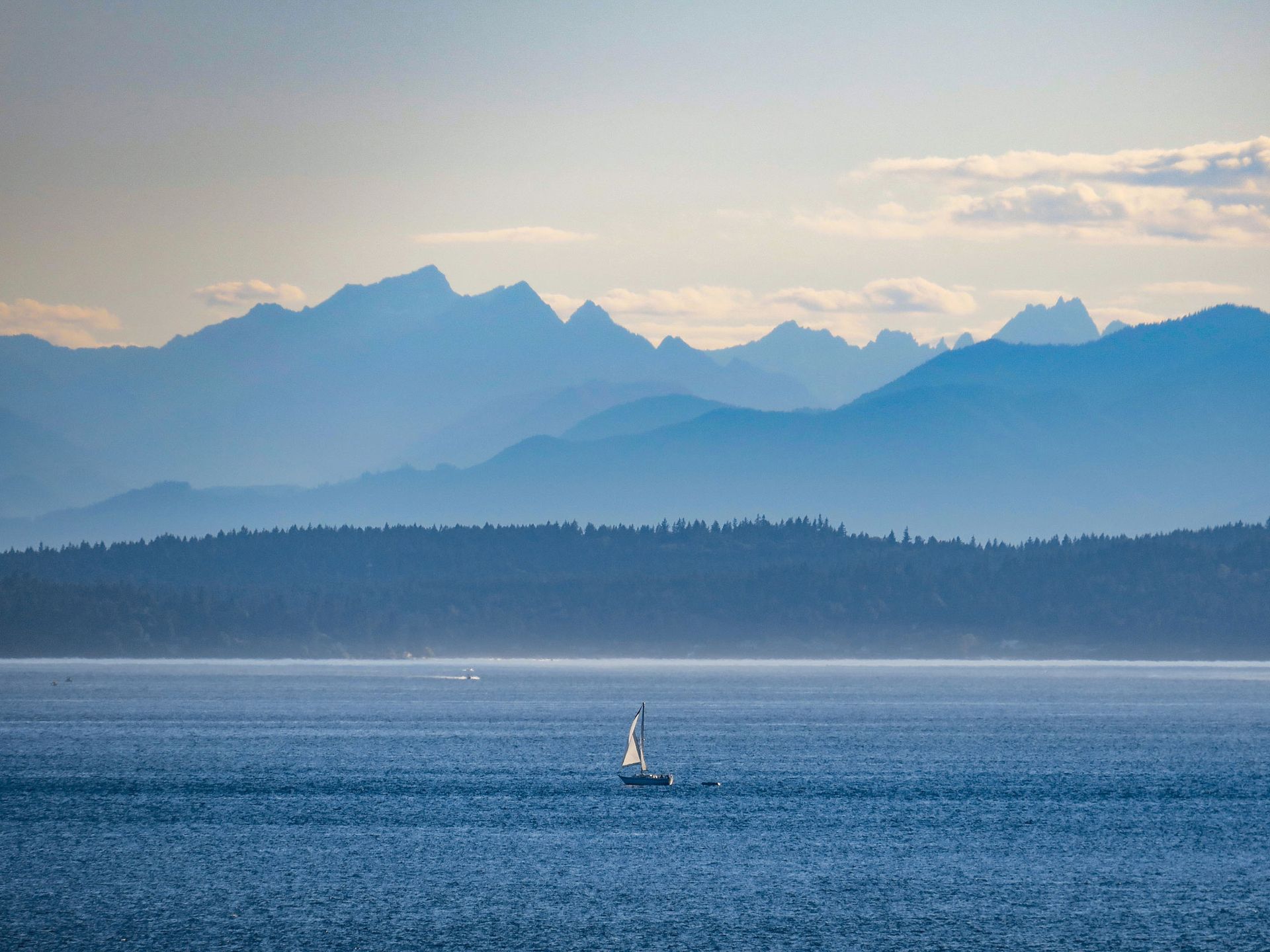 a sailboat is floating on top of a large body of water with mountains in the background .