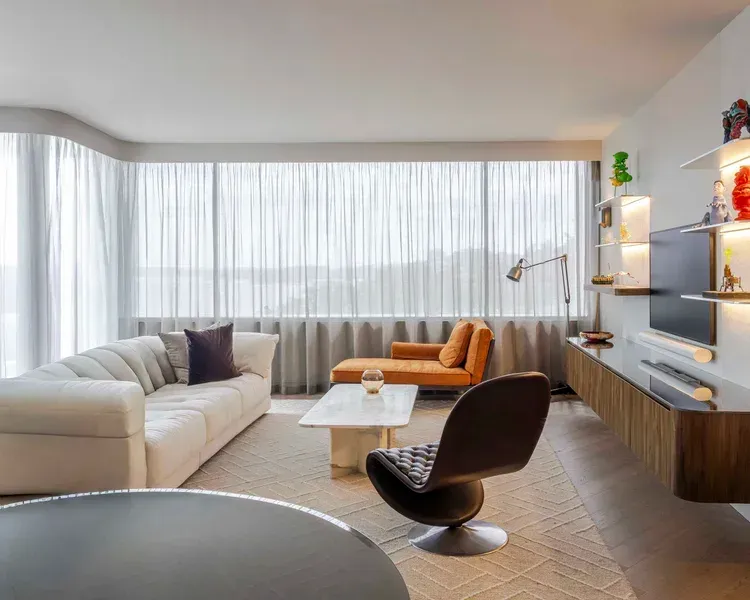 Modern living room with beige sofa, orange chairs, round lounge chair, and large windows with sheer curtains