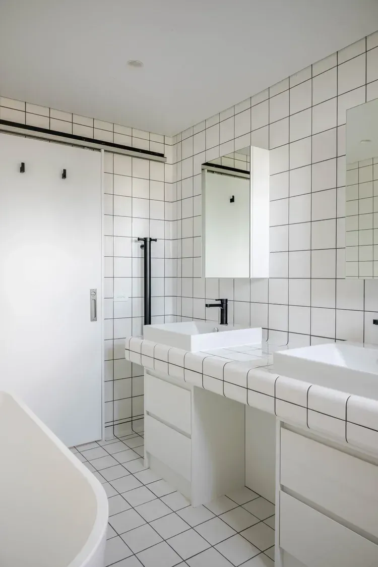 White tiled bathroom with bathtub, double sink vanity, and wall mirror