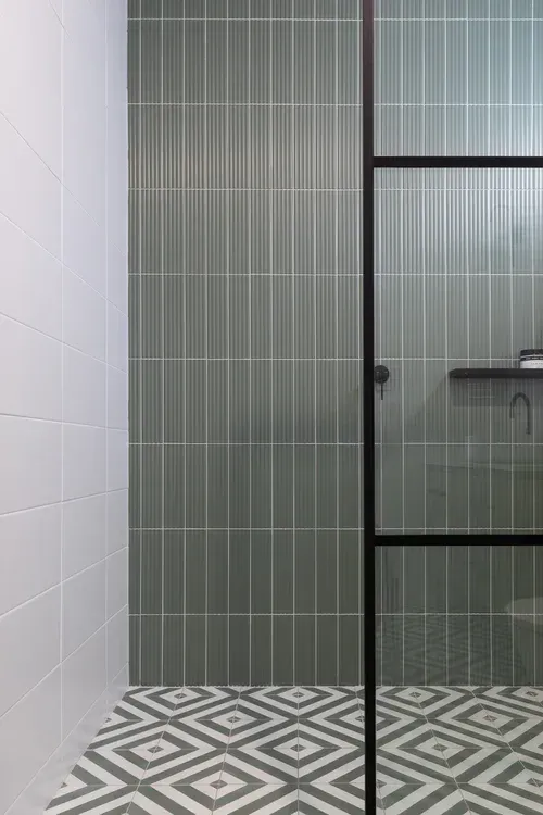 Modern bathroom with patterned tile floor, gray striped walls, and a glass shower door