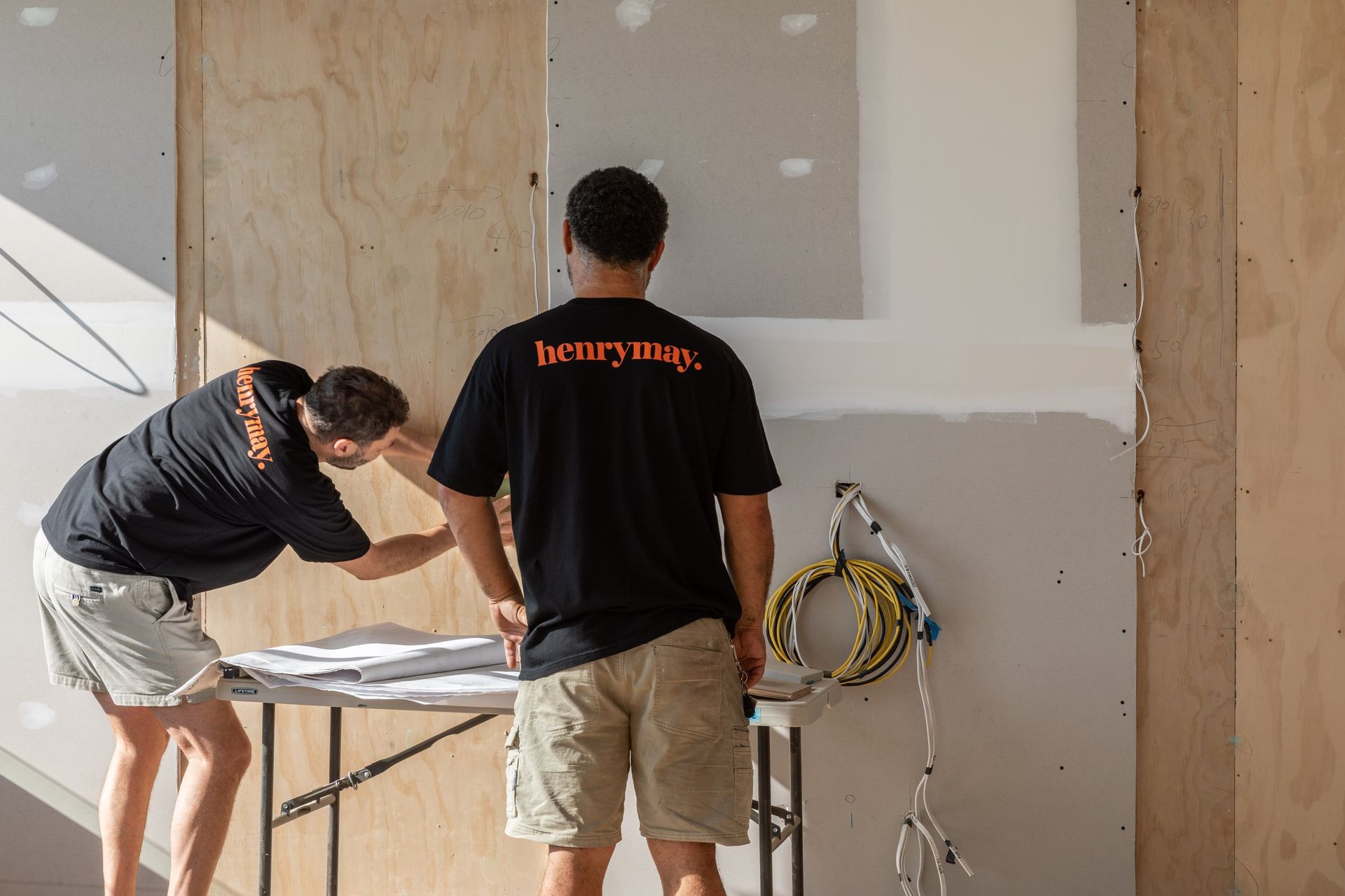 Two workers in a room, measuring a wall during home renovation.