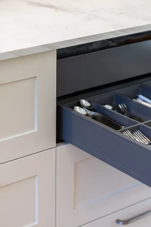 Open kitchen drawer with silver utensils beside a white cabinet and countertop