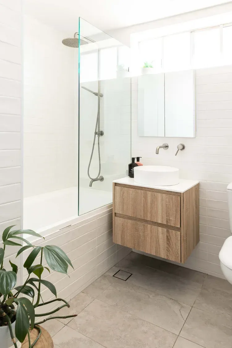 Modern bathroom with walk-in shower, floating wood vanity, white tiles, and a potted plant