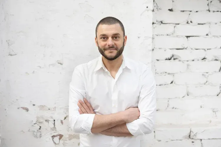 Man in a white shirt standing with arms crossed against a white brick wall