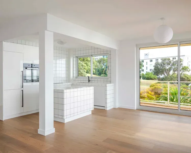 Bright modern open-plan room with white tile island, hardwood floors, and large sliding glass doors to a patio.
