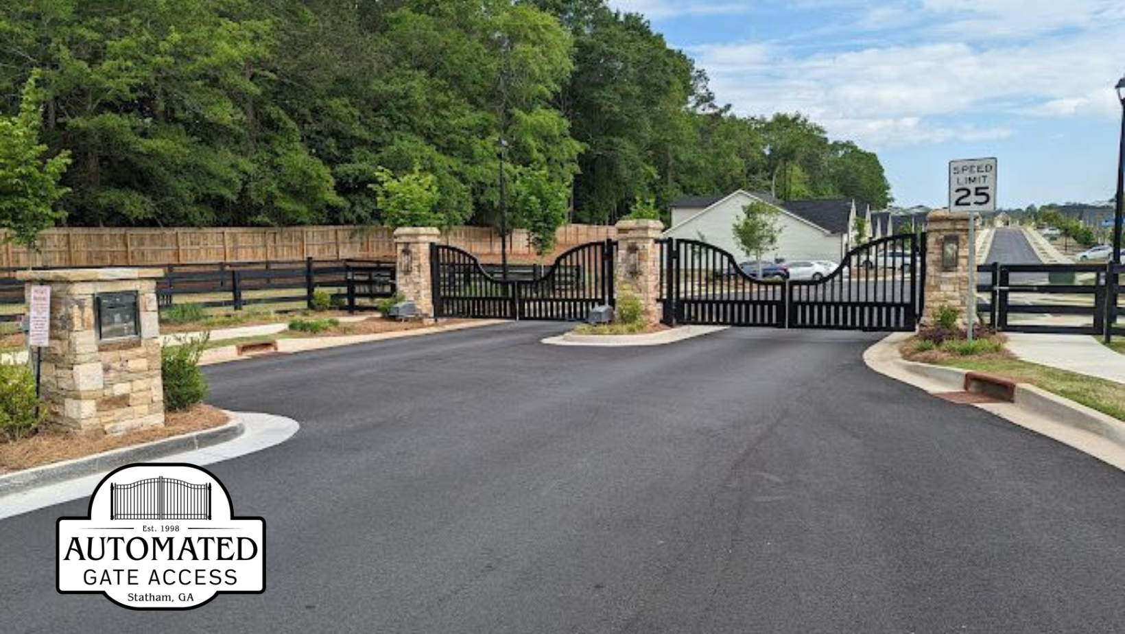 Gated entrance to a residential area with black wrought iron gates, stone pillars, and a speed limit sign.