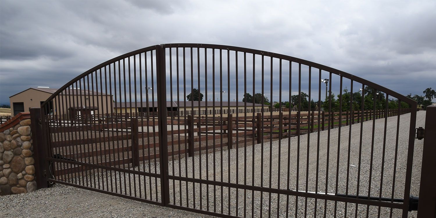 A large metal gate is open to a gravel driveway.