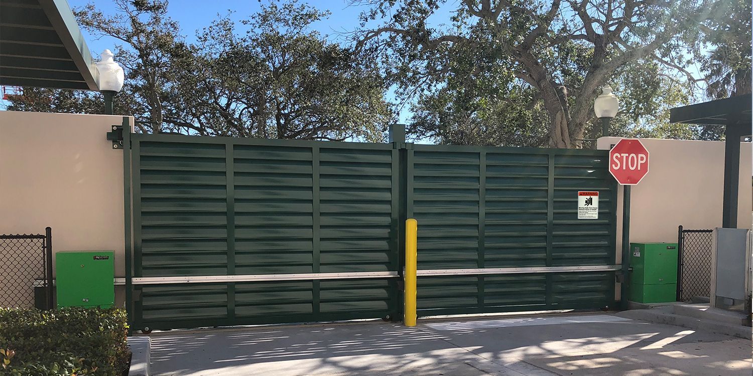 A large metal gate is open to a gravel driveway.