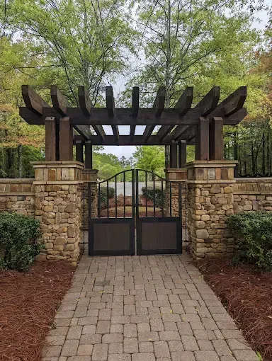 A brick walkway with a pergola and a gate leading to a house.