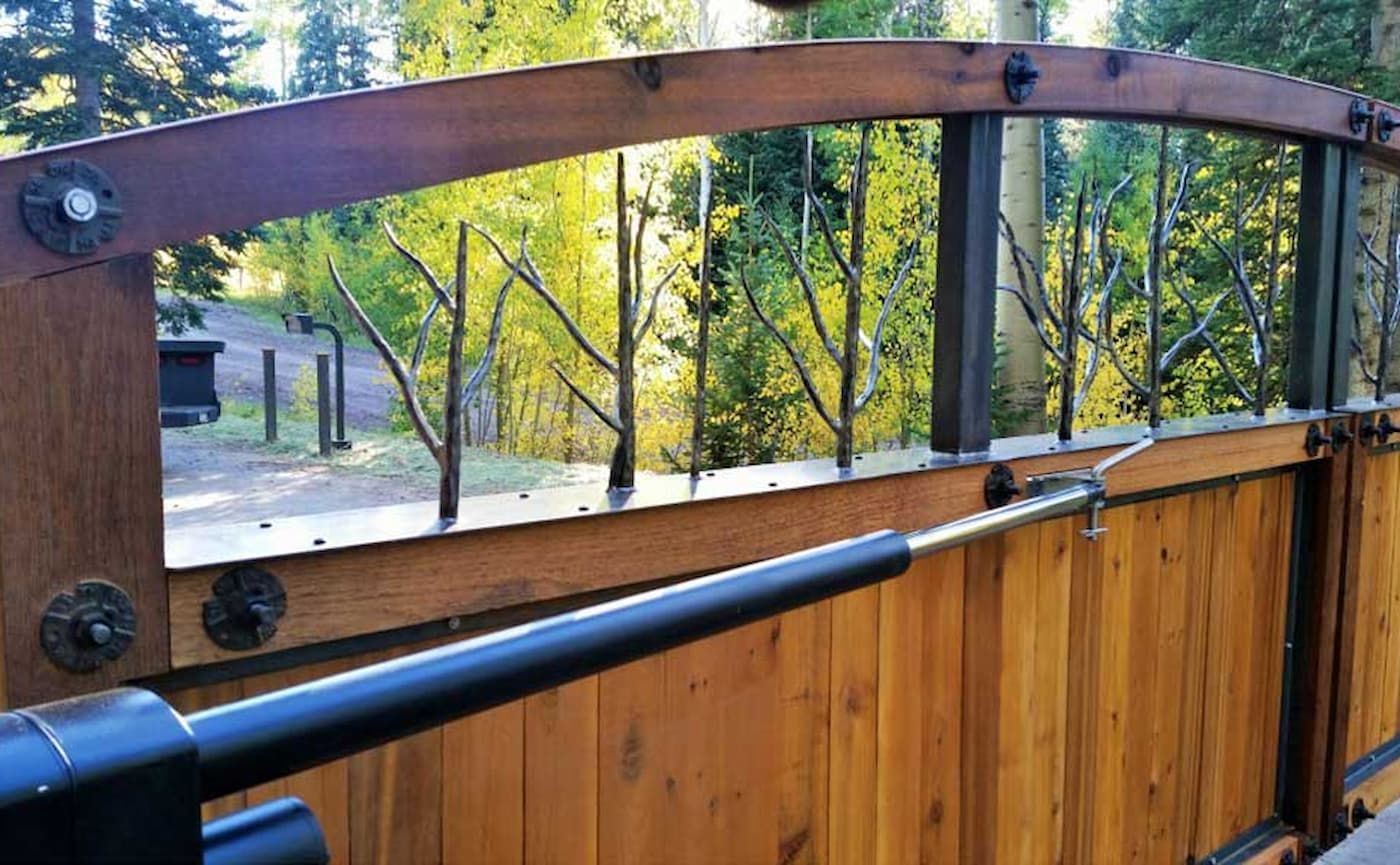 A wooden fence with a metal gate and trees in the background.