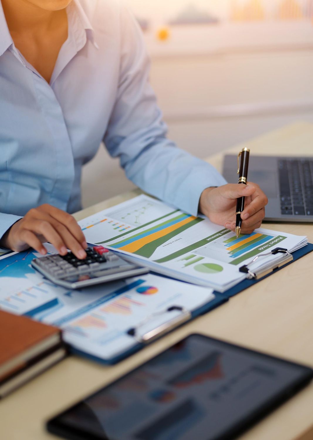 A woman is sitting at a desk using a calculator and writing on a clipboard.