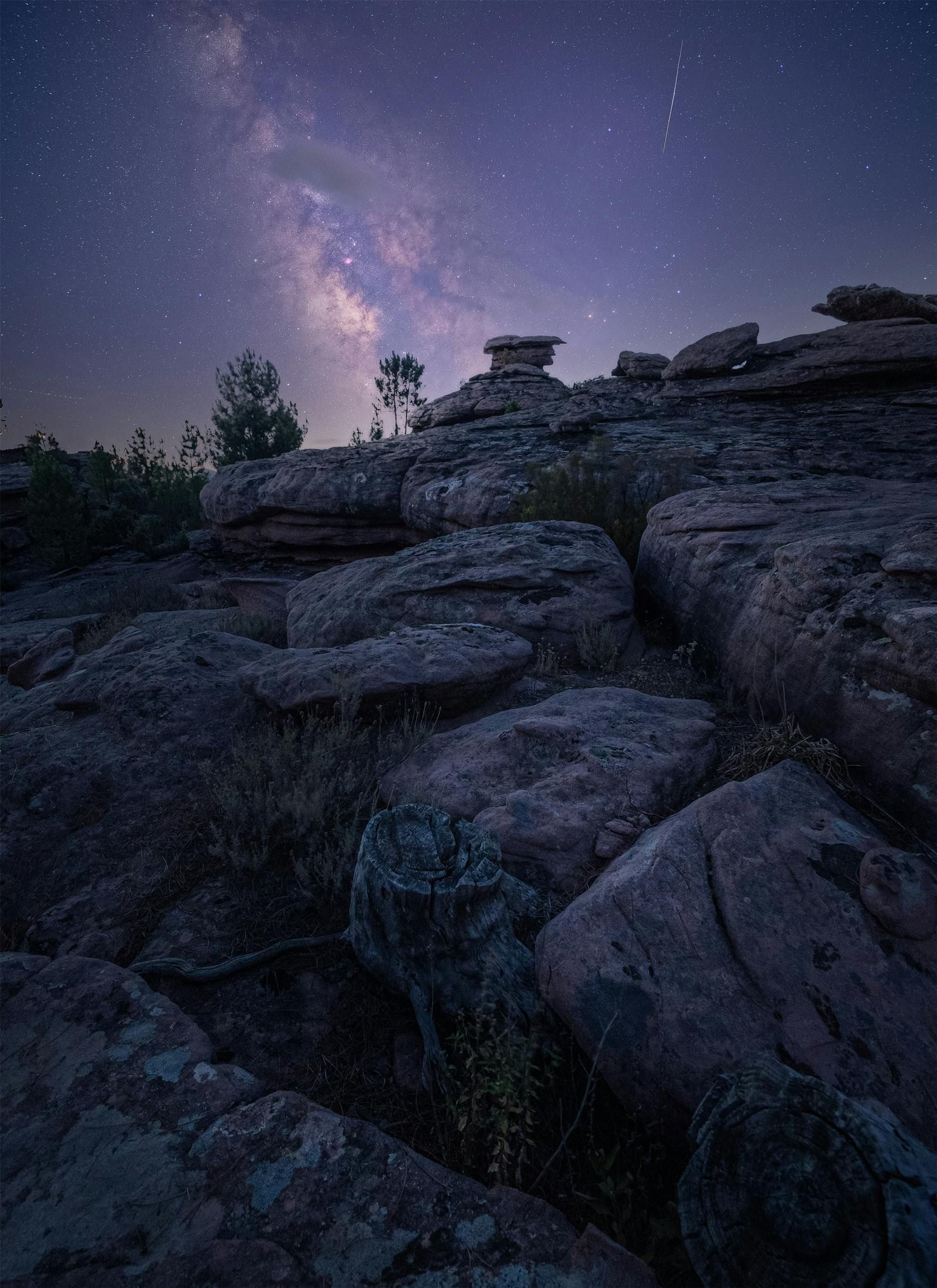 The milky way is visible over a rocky landscape at night.
