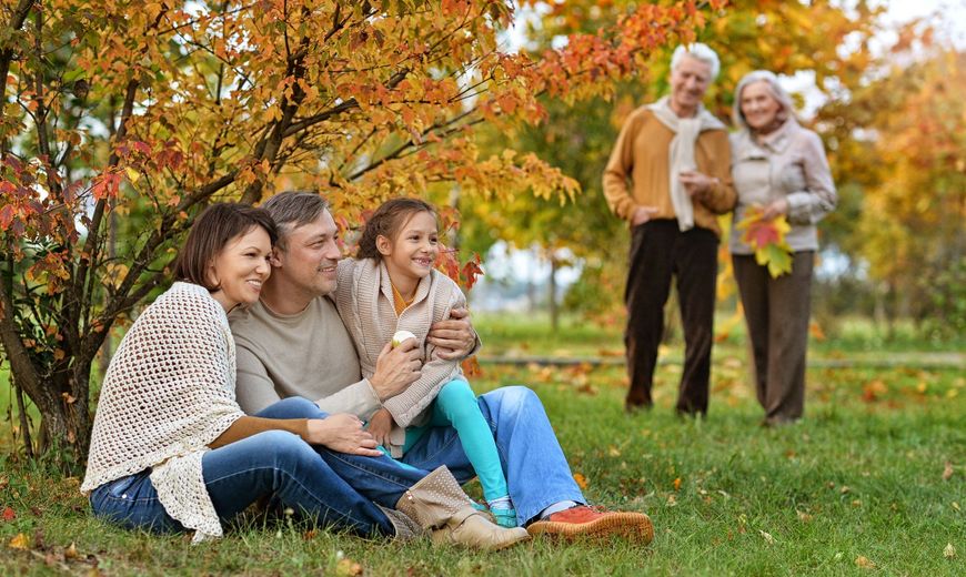 A family is sitting on the grass under a tree in a park.