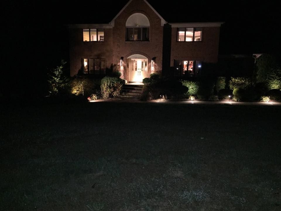 Night view of a brick house with landscape lighting illuminating the front yard and entrance.