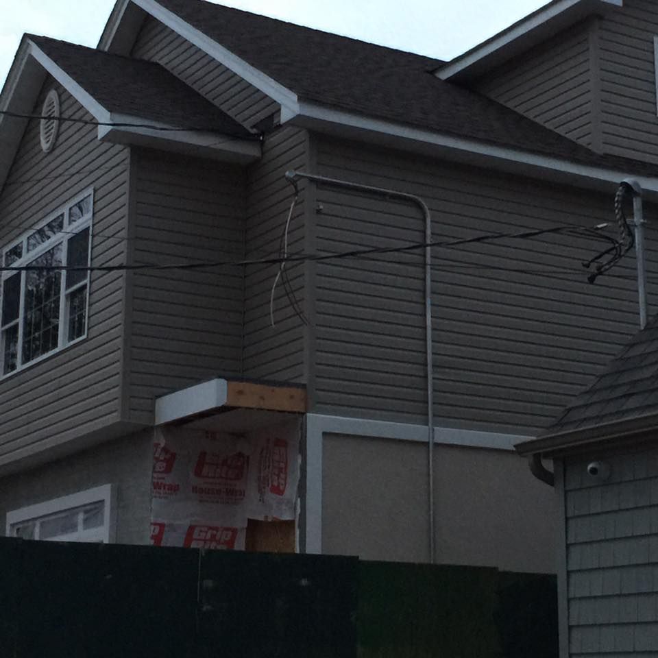 Two-story house with tan siding, brown roof, and utility pipes on the exterior.