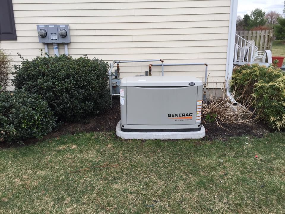 A Generac generator sits on a concrete pad beside a house.