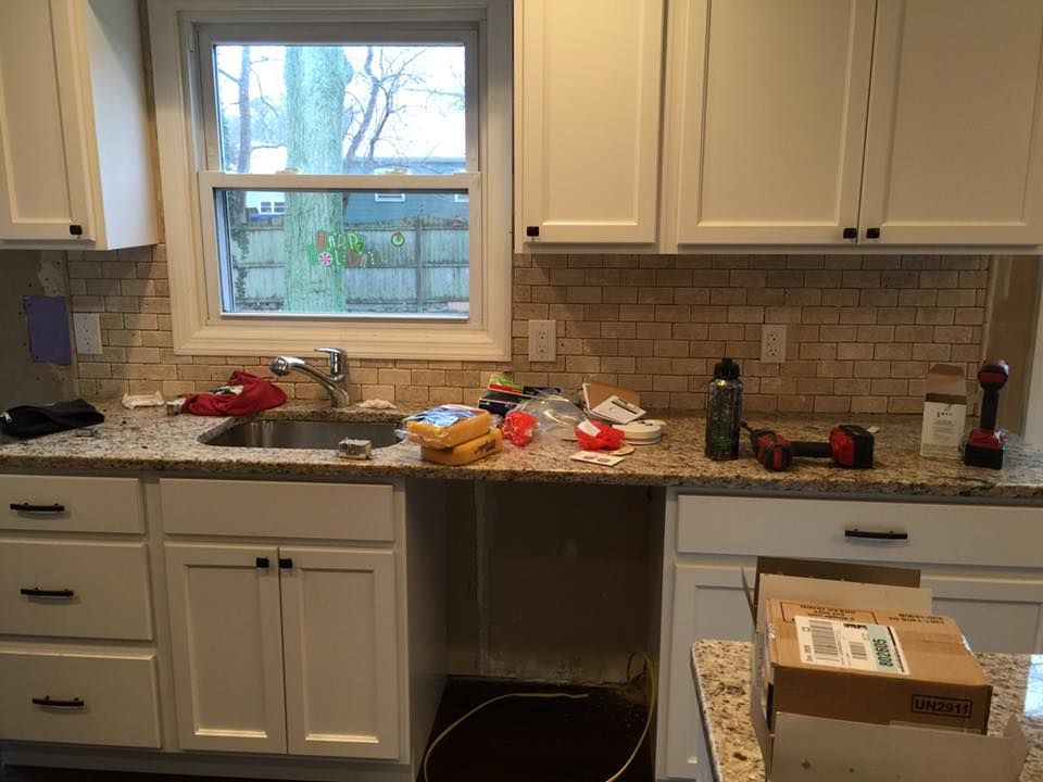 Kitchen under renovation with new cabinets, granite countertops, and backsplash. Tools and materials scattered around.