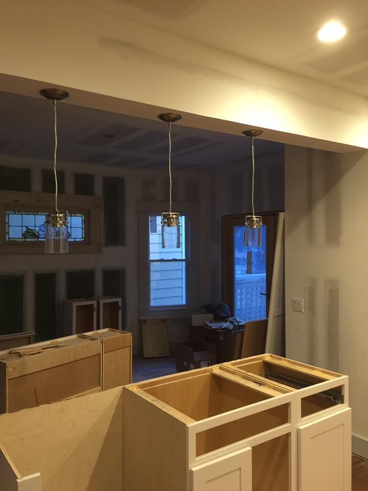 Kitchen under construction with pendant lights, cabinets, and a view to another room with windows.