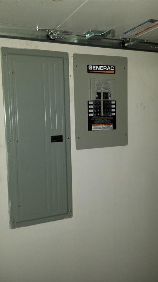 Two electrical panels on a white wall: a gray circuit breaker panel, and a gray Generac panel.
