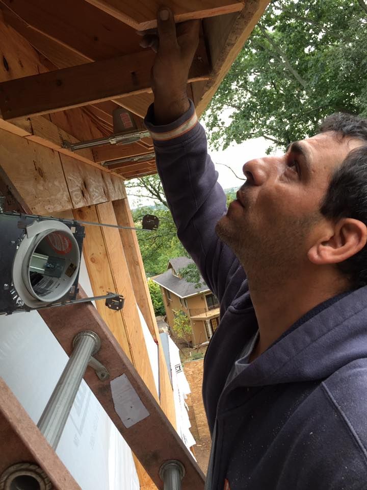 Man on ladder, installing wooden trim on house exterior. He's looking up, hand on the wood.