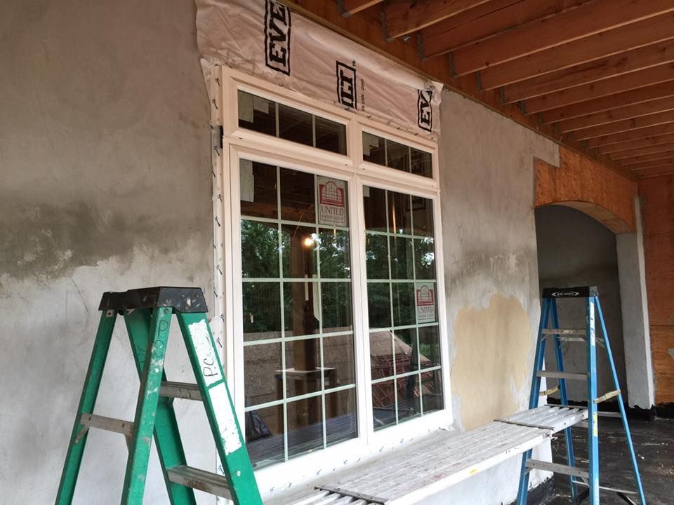 Construction site: window installation with a green ladder and scaffolding. Exterior wall with stucco, unfinished.