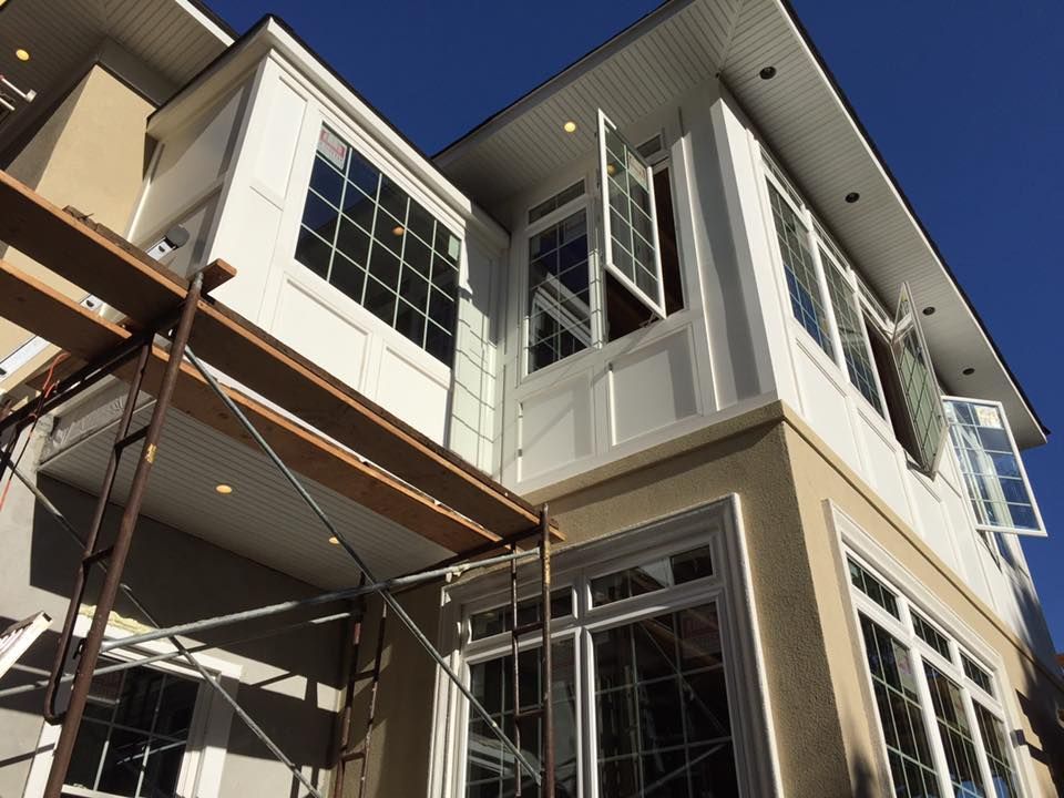 Exterior view of a house with white trim, beige stucco, and windows partially open; scaffolding present.