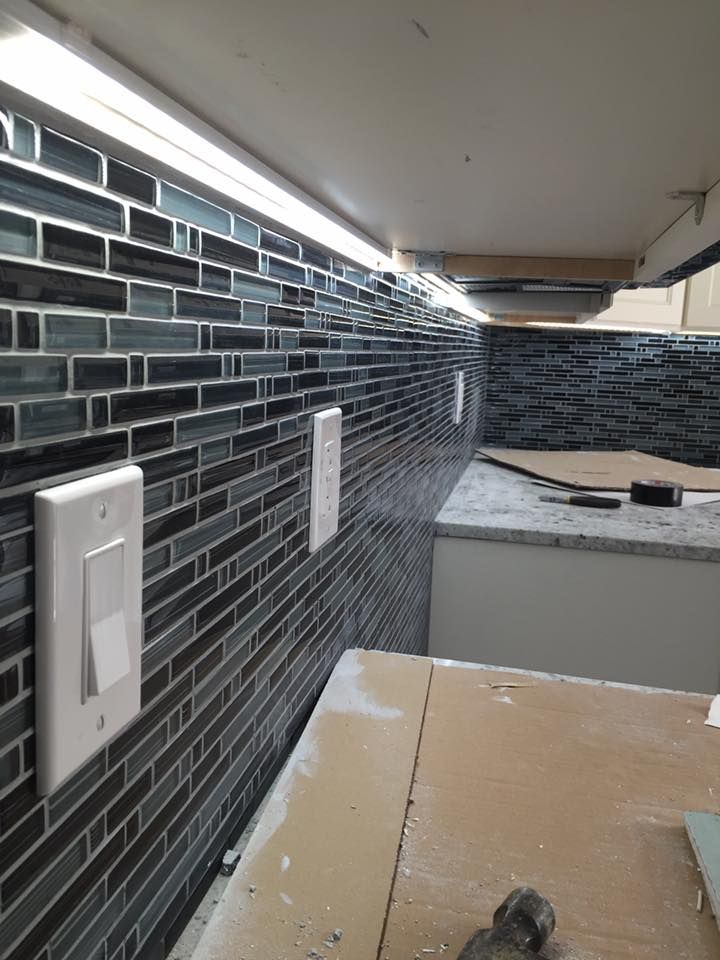 Kitchen backsplash with dark, rectangular tiles and white electrical outlets. Under-cabinet lighting illuminates the space.