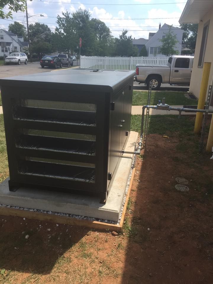 Dark gray electrical box on a concrete pad, next to a building and a grassy area with a street view.