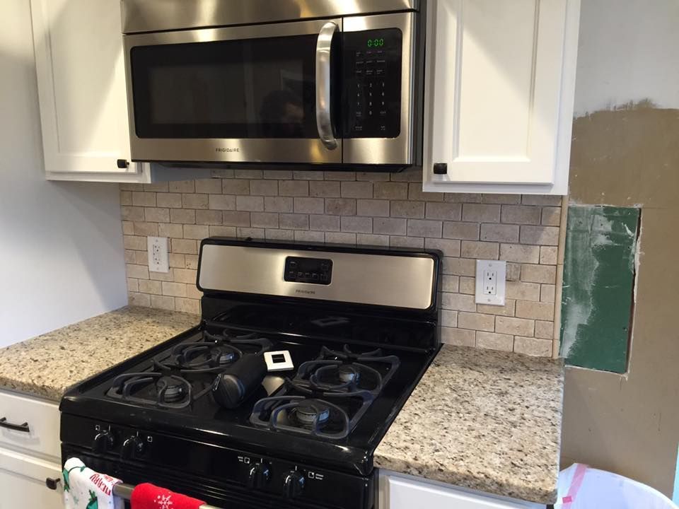 Kitchen with a stovetop, microwave, and tiled backsplash. A wall section is under construction.