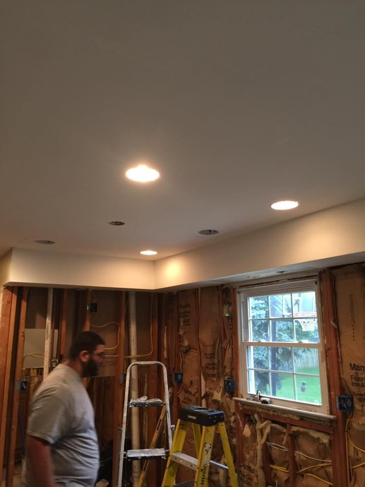 Man observing a kitchen renovation; exposed walls, recessed lights, ladder, and window.