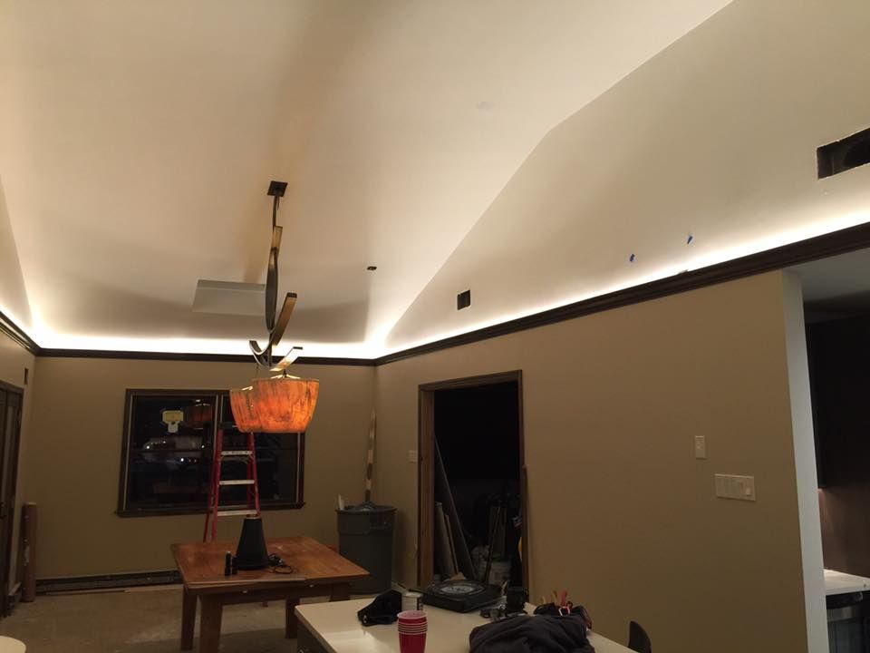 Room with recessed LED lighting; neutral walls, dark trim, and vaulted ceiling. A dining table and chandelier are visible.