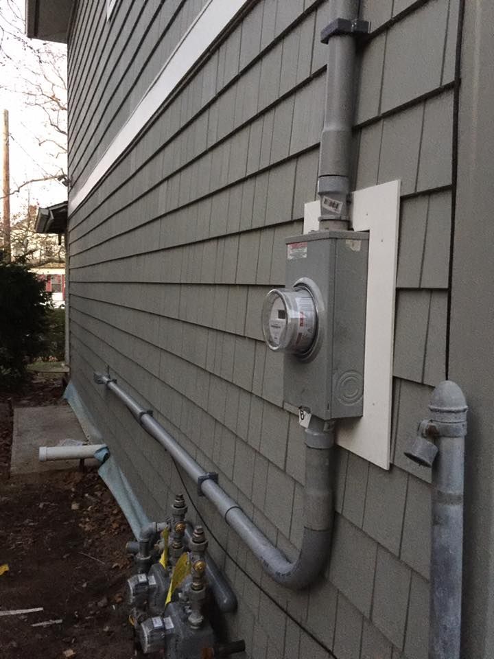 Exterior view of a house with a gray electrical meter and gas pipes on gray siding.